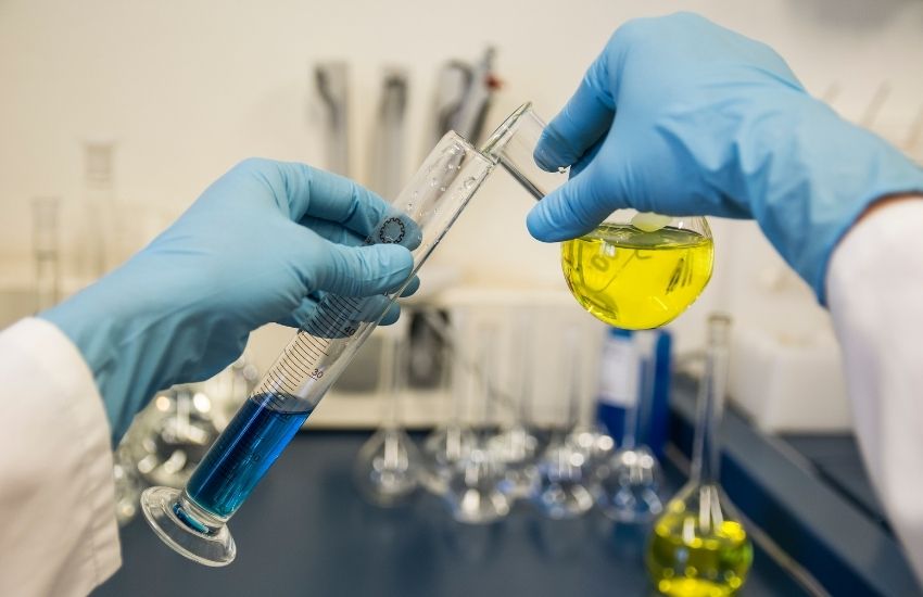 Laboratory technician wearing blue gloves conducting chemical analysis with blue and yellow liquids in glassware, representing research and innovation at Pozitron Chem Tech Pvt. Ltd.